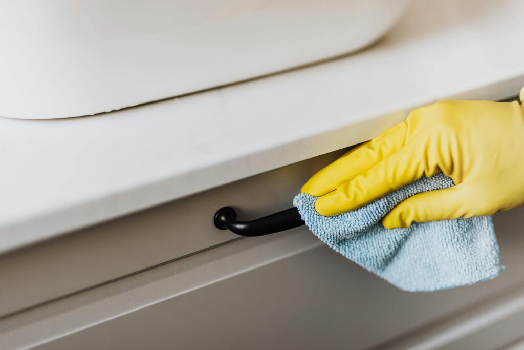 A woman cleaning a black drawer handle with a blue cloth.
