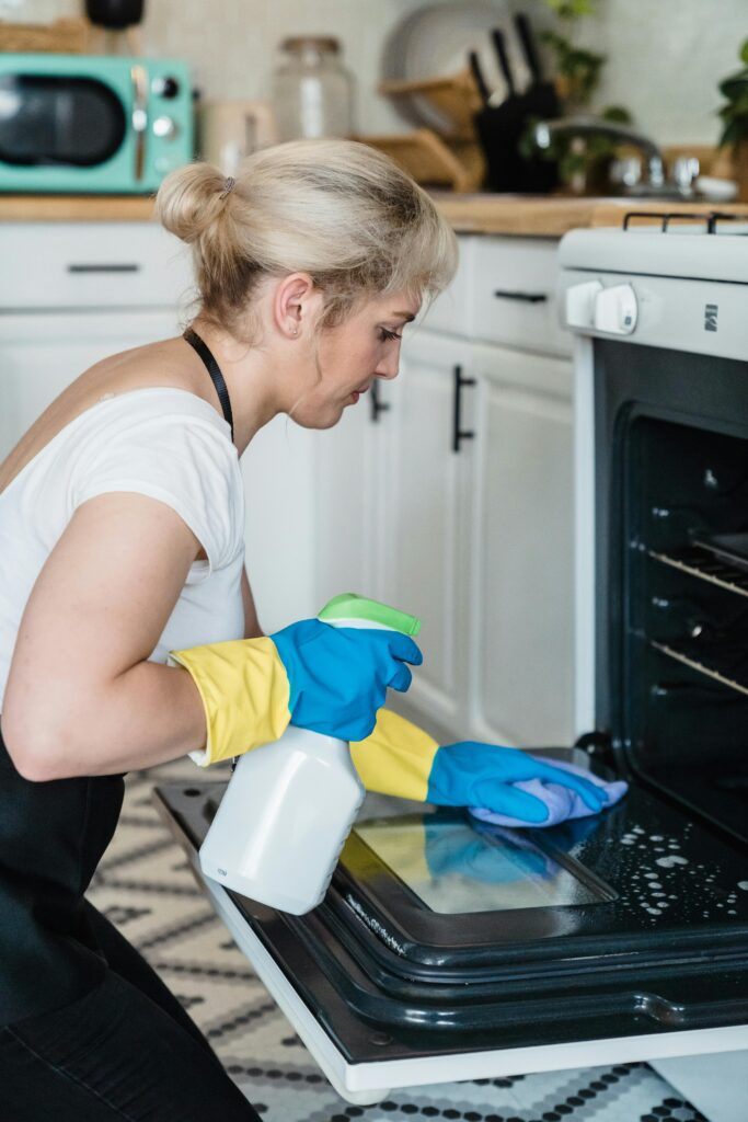 A cleaning lady with cleaning spray bottle in one hand cleaning oven mirror.